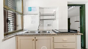 A kitchen with a double sink, a stove, and a built-in oven. There is a window with blinds, a towel rack, and a cabinet with drawers. - Catalan Loft Retreat (Alghero)