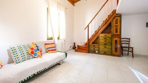 A living room with a sofa, colorful pillows, a staircase, and a wooden cabinet. - Catalan Loft Retreat (Alghero)