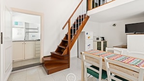 A compact kitchen with wooden stairs, a dining table with chairs, and a television on the wall. - Catalan Loft Retreat (Alghero)