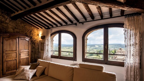 A cozy room with a sofa, a wooden cabinet, and three arched windows offering a view of the countryside.