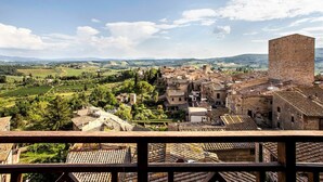 A historic town with terracotta-roofed buildings, a prominent tower, and rolling hills in the background.