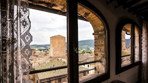 A room with a large arched window overlooking a historic town with old buildings and a tower.