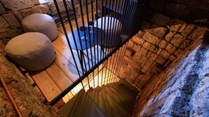 A stone-walled staircase leading to a lower level with a wooden floor and a metal railing.