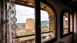 A room with a large arched window overlooking a historic town with old buildings and a tower.