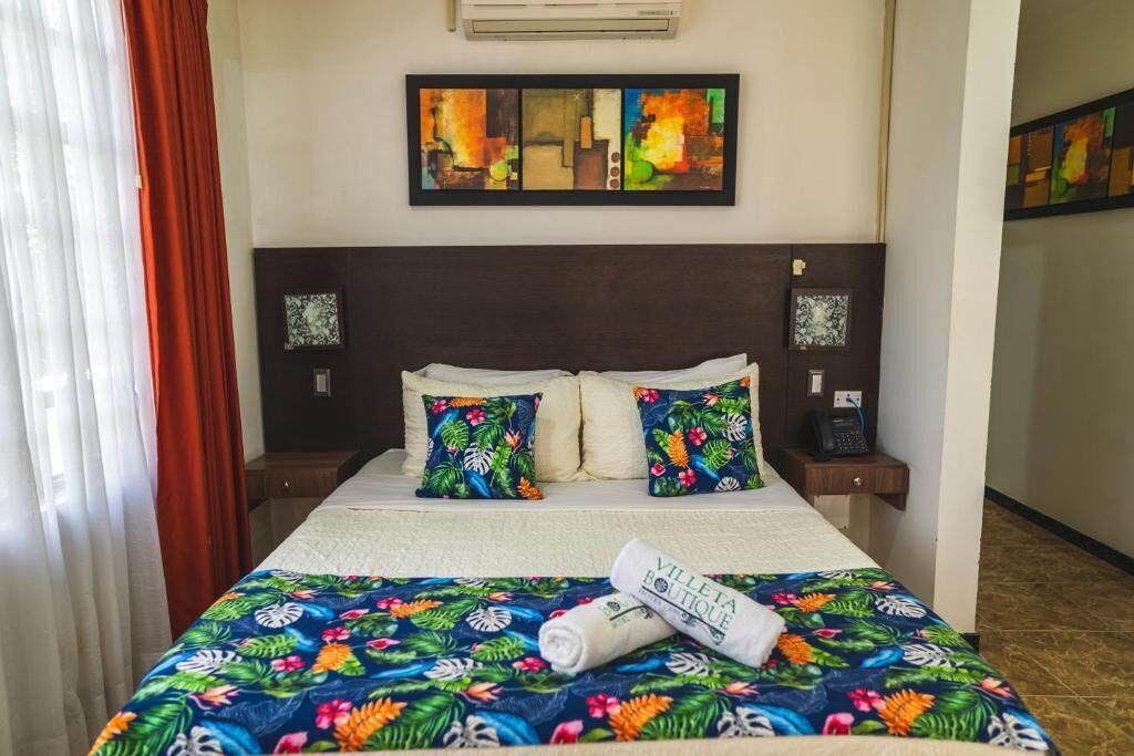 A hotel room with a bed, two pillows, a nightstand, a phone, and a wall art piece.