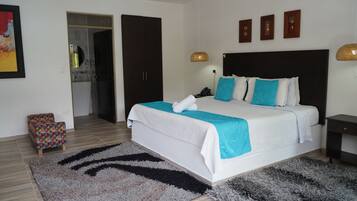 Un dormitorio moderno con una cama grande, una mesita de noche pequeña, una mesita auxiliar y una puerta que da a un baño.