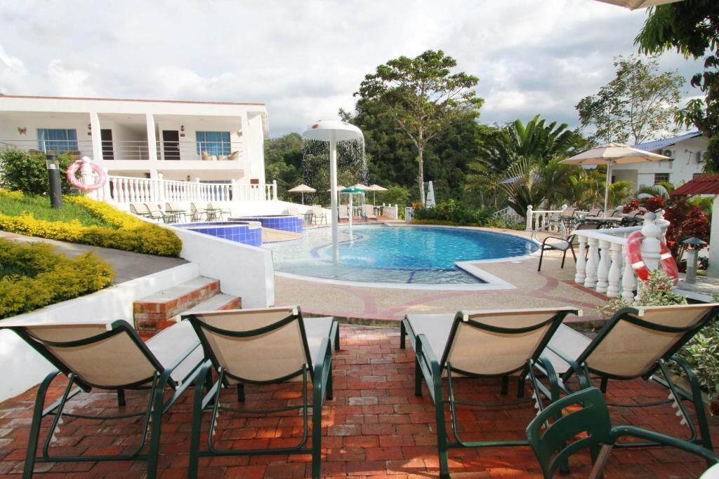 A pool area with lounge chairs, a water fountain, and a building with balconies.
