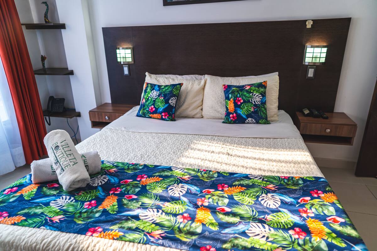 Una habitación de hotel con una cama, dos mesitas de noche y un aparador.