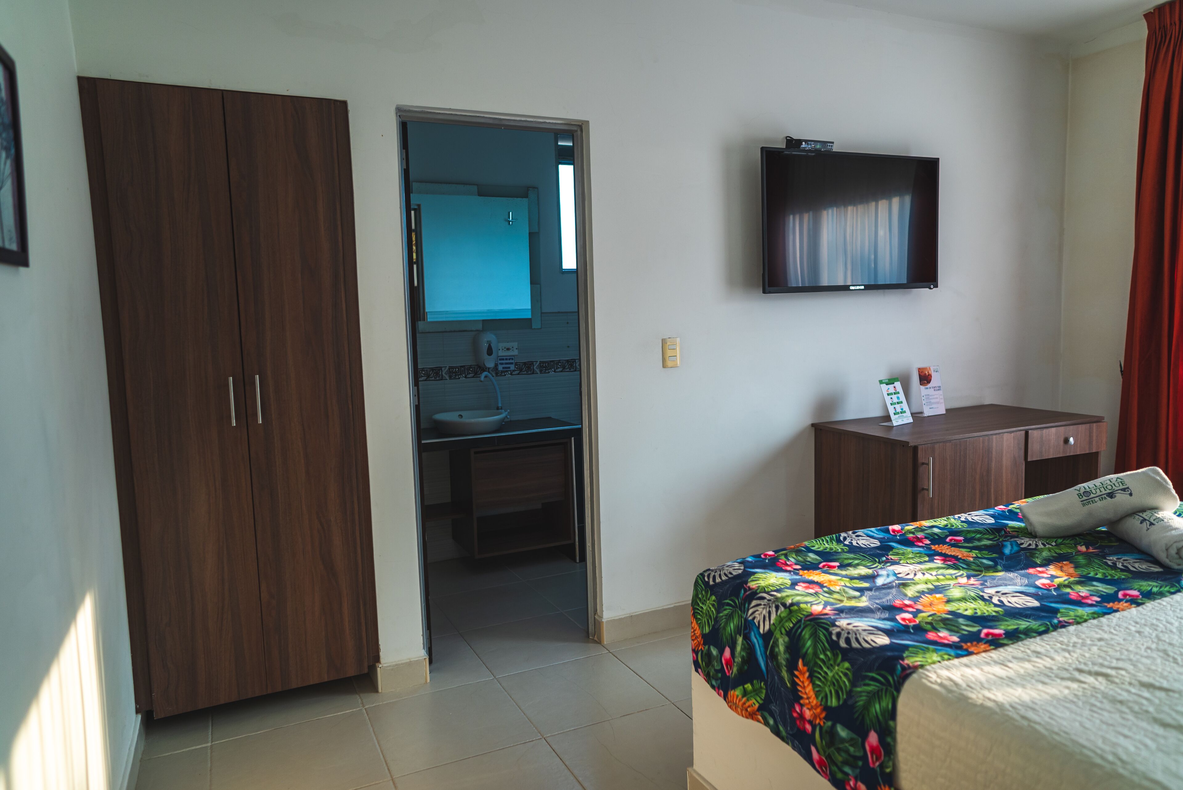 A hotel room with a bed, a wardrobe, a television, and a bathroom visible through an open door.