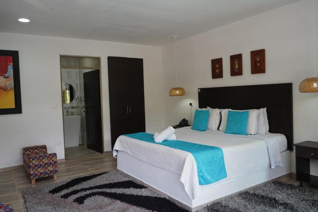 Una habitación de hotel moderna con una cama grande, un pequeño rincón de descanso y un baño visible a través de una puerta abierta.
