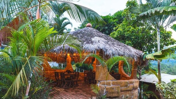A thatched-roof structure with outdoor seating, surrounded by lush tropical vegetation.