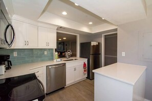 A modern kitchen with white cabinets, a stainless steel refrigerator, a dishwasher, and a black stove.