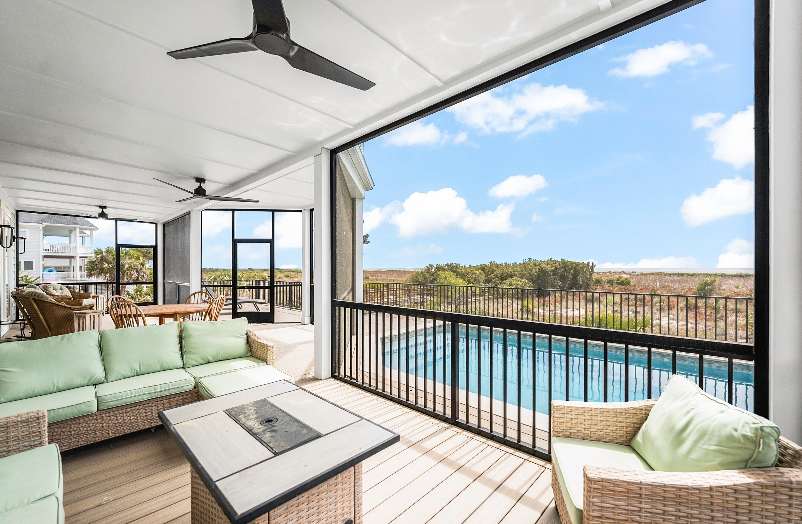 A covered outdoor area with a pool, wicker furniture, ceiling fans, and a view of the landscape.