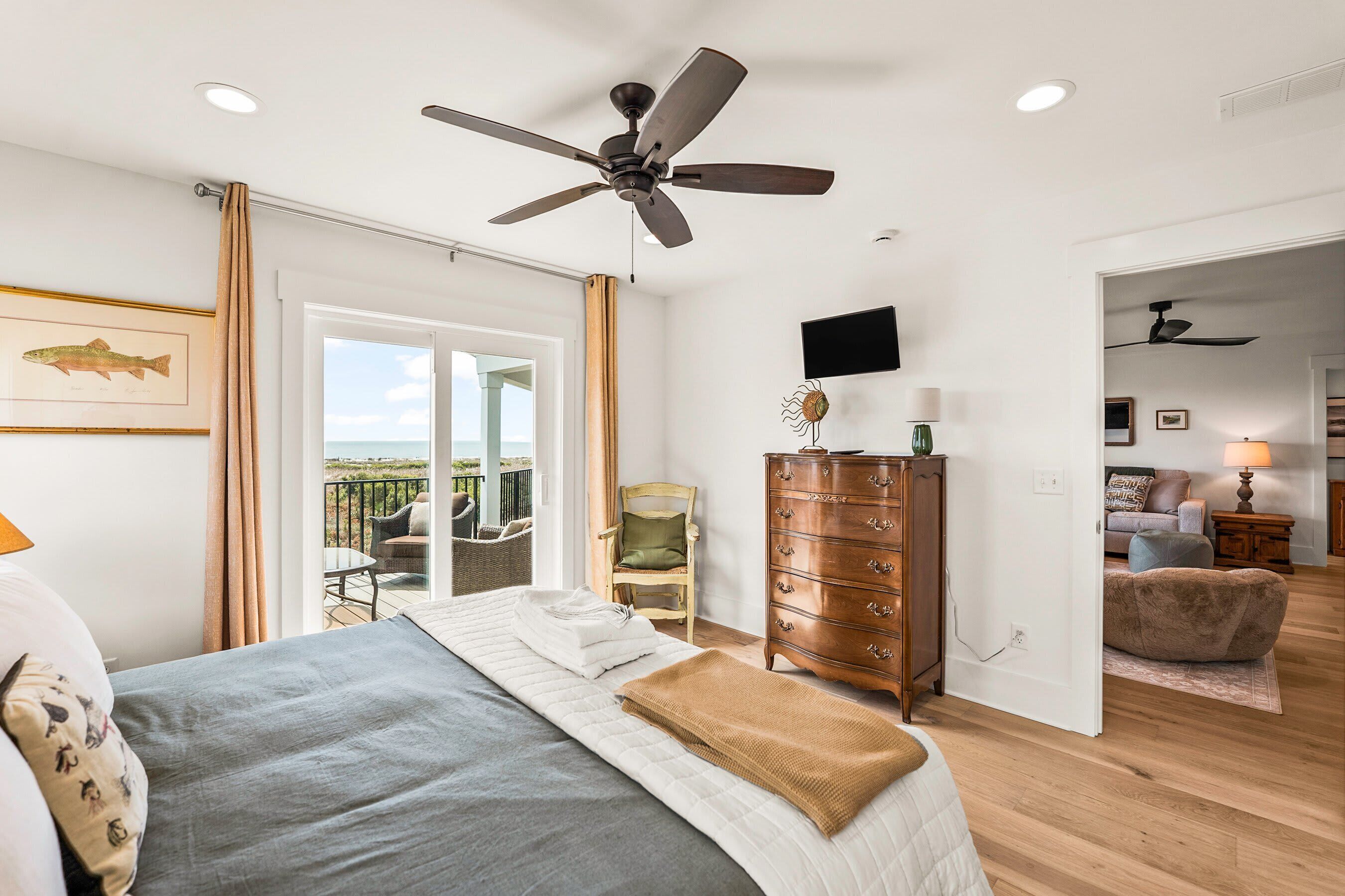 A bedroom with a bed, a dresser, a television, and a balcony with outdoor furniture.