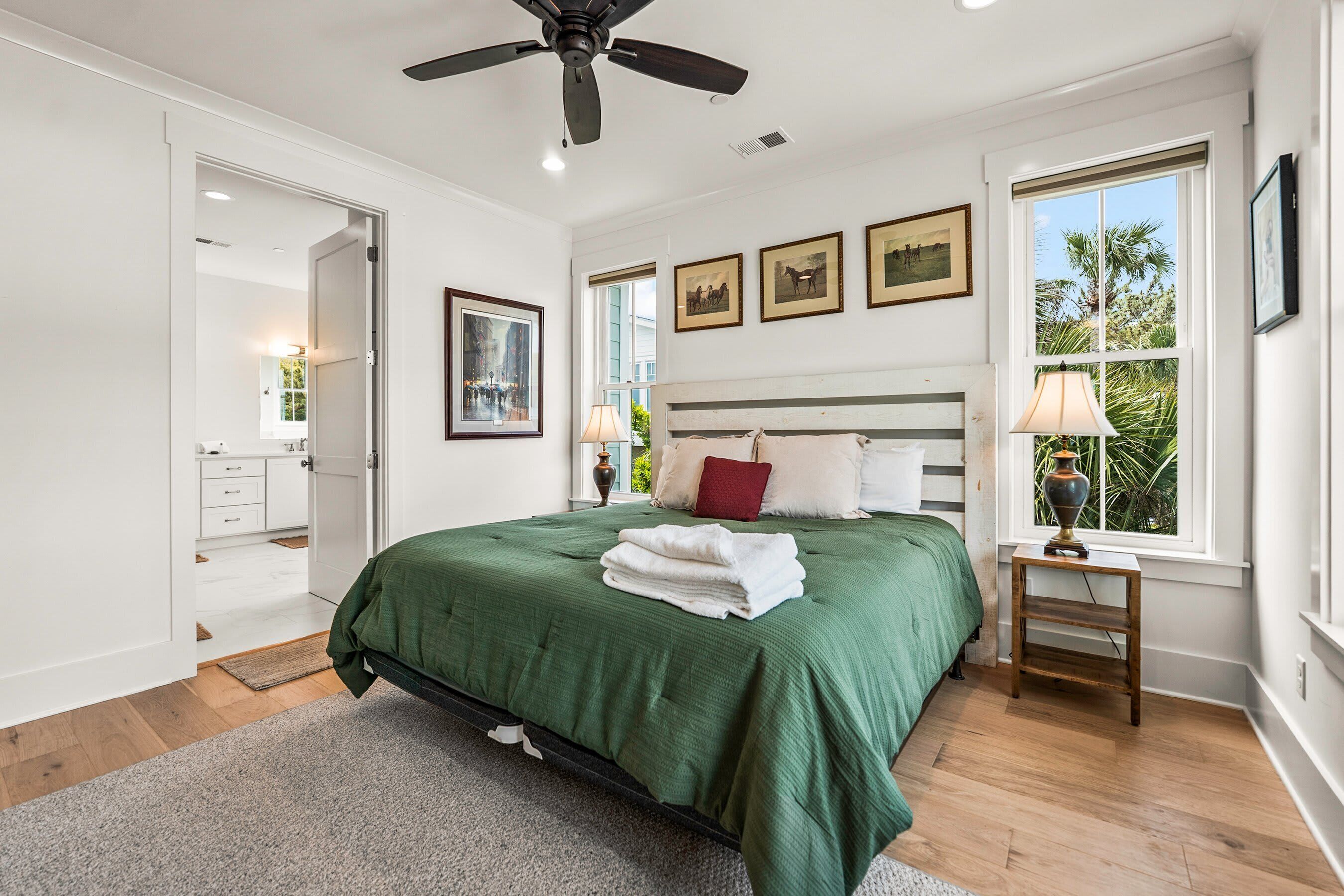 A bedroom with a bed, a ceiling fan, a window with a view, and a door leading to another room.