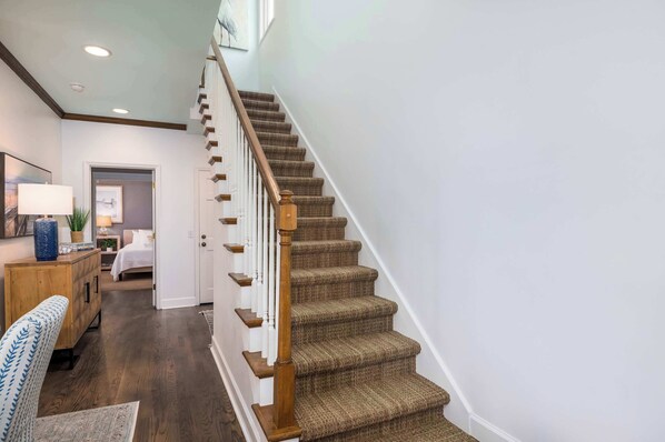 A staircase with wooden steps and a handrail, leading to a bedroom with a bed and a nightstand.