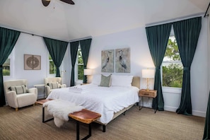 A bedroom with a large bed, two armchairs, a wooden nightstand, and a small table.