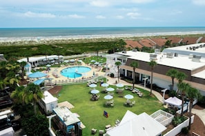 Une piscine située sur le toit, offrant une vue sur la plage, entourée de palmiers et dotée d’un espace salon extérieur.
