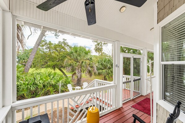 A covered porch with a view of a lush garden, white railings, and a red carpet.