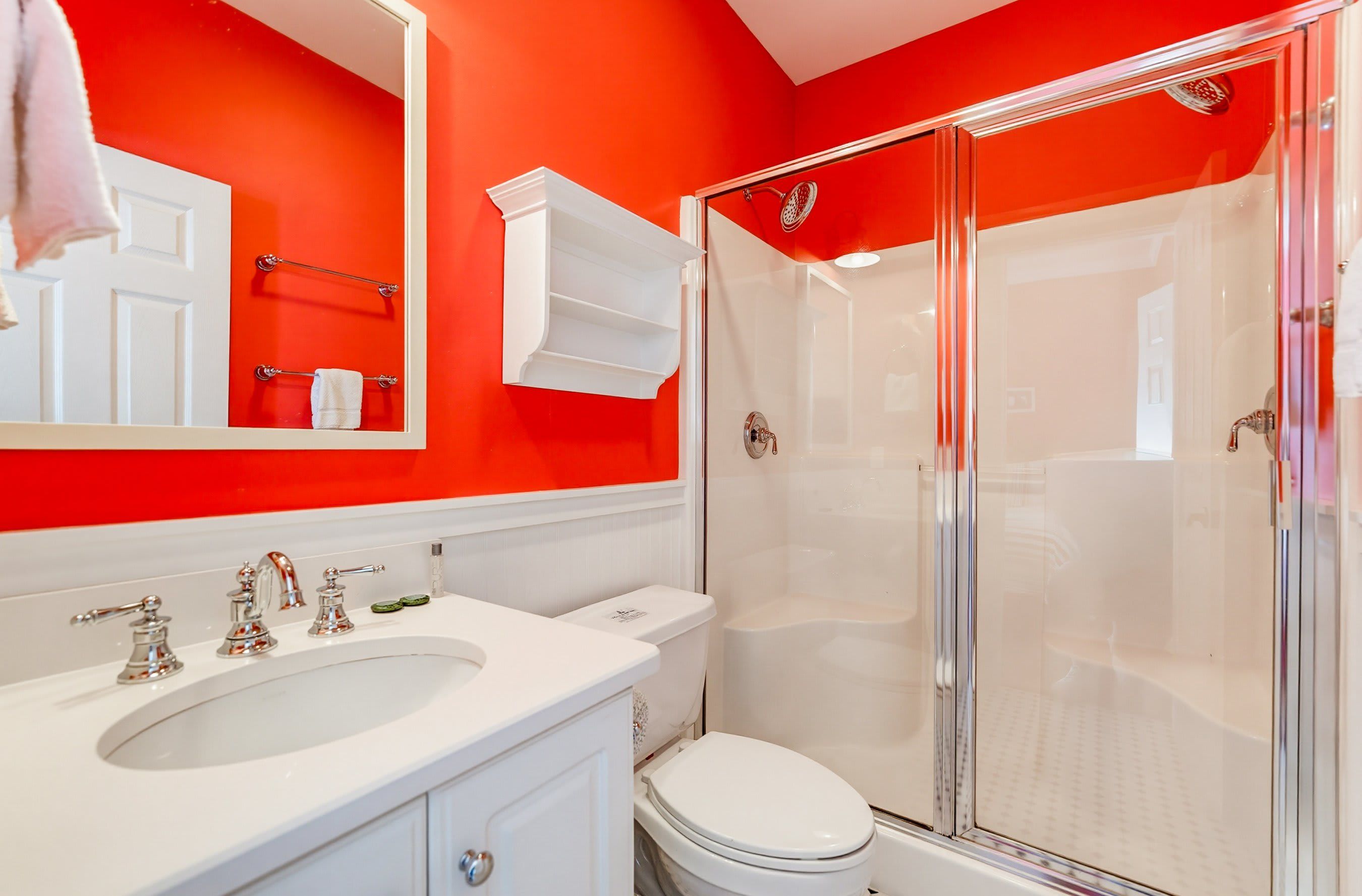 Une salle de bain avec un lavabo blanc, deux robinets, des toilettes et une douche à parois de verre.