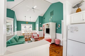 A room with teal walls, a ceiling fan, a dining area with chairs and a table, and a white refrigerator.