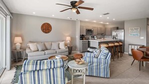 A modern living room with a sofa, striped armchairs, a small round table, and a ceiling fan.