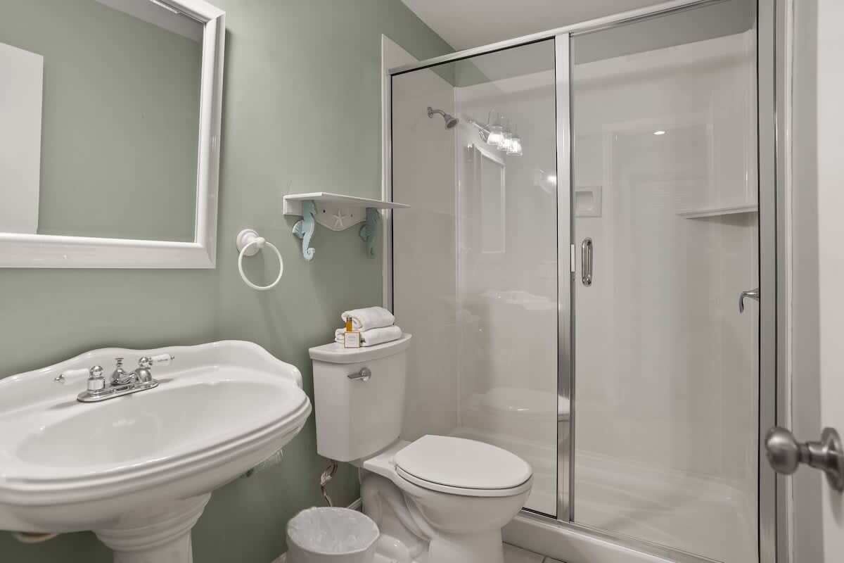 A bathroom with a pedestal sink, toilet, and a glass-enclosed shower.