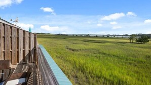 A wooden deck with a view of a grassy field and a body of water.
