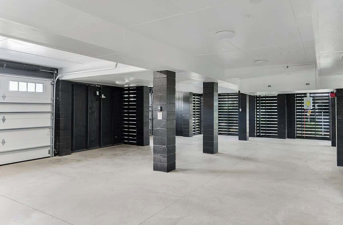 A spacious indoor area with a large garage door, multiple black metal gates, and concrete pillars.