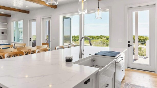 A modern kitchen with a large island, pendant lights, and a view of the outdoors. - 718 Swordfish Road (Fripp Island)