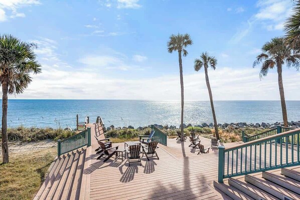 A wooden deck with chairs and a table overlooking the ocean, palm trees, and a clear sky. - 657 Newhaven (Saint Helena Island)