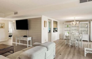 A living room with a flat-screen TV, a sofa, a coffee table, and a dining area with a chandelier. - 657 Newhaven (Saint Helena Island)