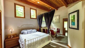 A bedroom with a bed, bedside table, lamp, and a dining area with chairs and a table.