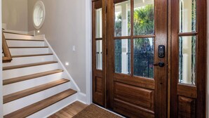 Un escalier en bois, un mur blanc, une porte en bois avec des panneaux de verre et un petit miroir rond accroché au mur.