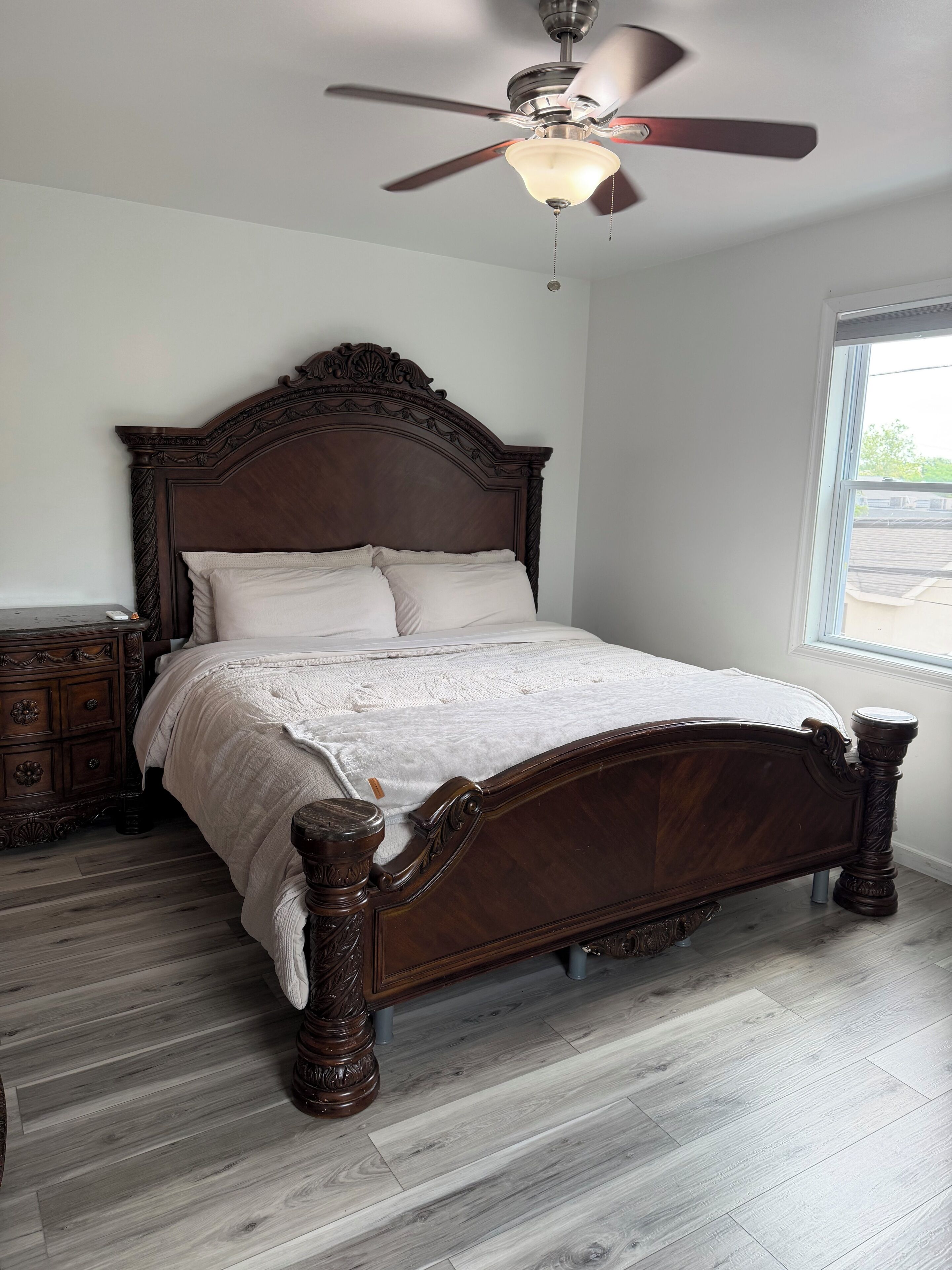 A bedroom with a wooden bed, a nightstand, a dresser, and a ceiling fan.