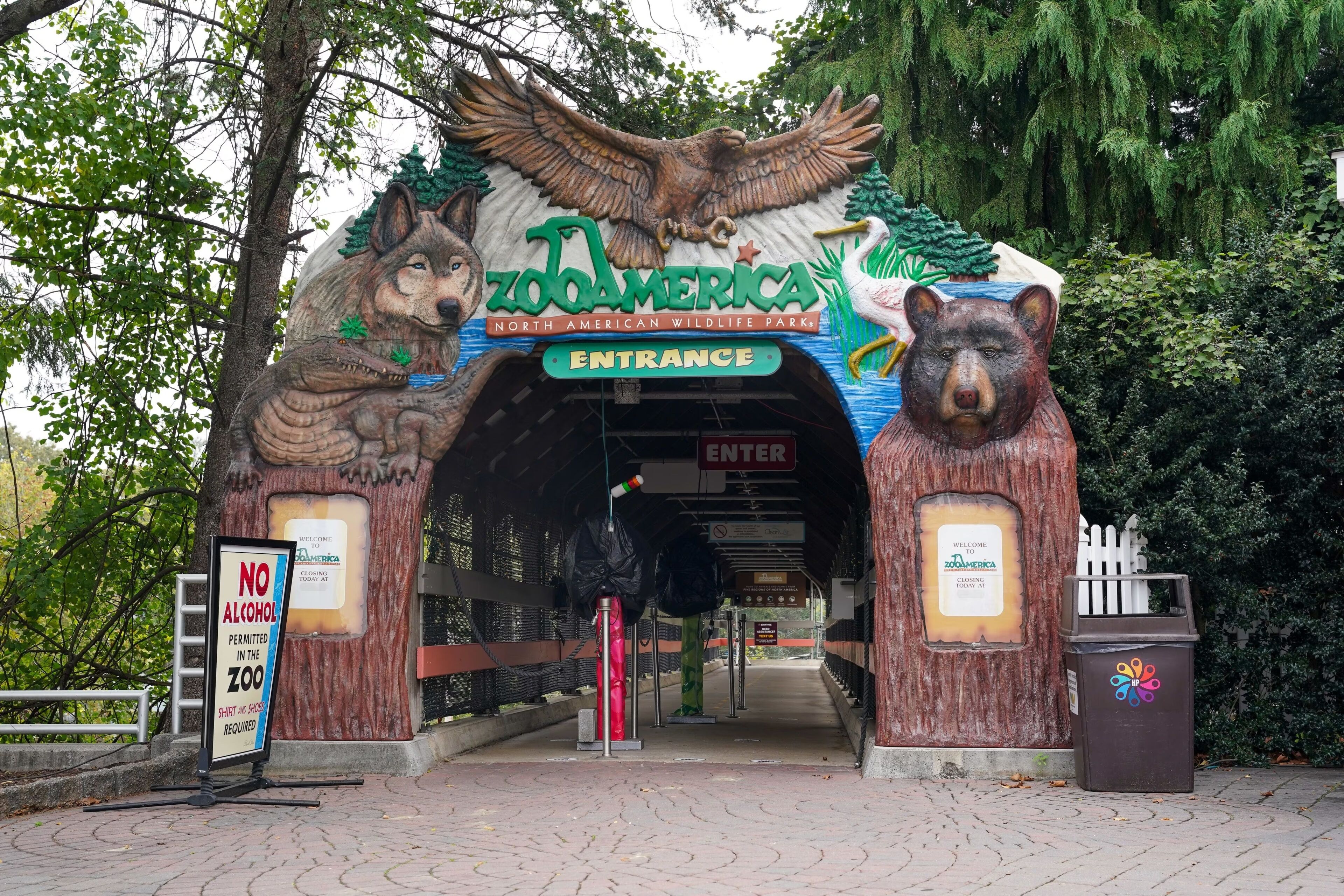 L’entrée du zoo ZooAmerica est marquée par une grande sculpture représentant un ours et un loup, un panneau indiquant qu’il est interdit de consommer de l’alcool et une poubelle.