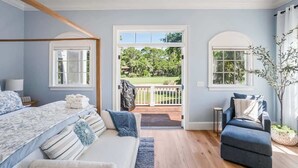 A bedroom with a bed, a sofa, a chair, and a view of a garden through a door. - 778 Marlin Drive (Fripp Island)