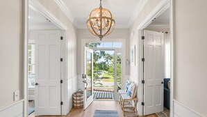 A hallway with a chandelier, white doors, a view to the outside, and a bench with cushions. - 778 Marlin Drive (Fripp Island)