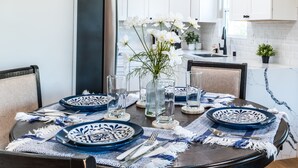 Ein Esstisch ist gedeckt mit blauen und weißen Tellern, einer Vase mit weißen Blumen und einem Glas Wasser.