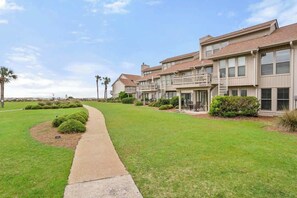 A multi-story residential building with a paved walkway, manicured lawns, and a clear sky. - 111 Capt John Fripp Villa (Fripp Island)