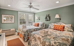 A bedroom with two beds, a ceiling fan, a window with blinds, wall-mounted lamps, and a framed picture. - 111 Capt John Fripp Villa (Fripp Island)