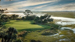 A golf course with a water body in the background, surrounded by trees and vegetation. - 111 Capt John Fripp Villa (Fripp Island)