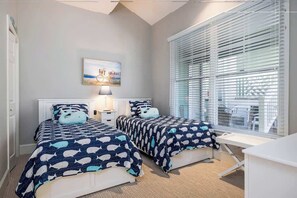 Ein Schlafzimmer mit zwei Betten, einem Nachttisch, einer Lampe, einem Fenster mit Jalousien und einem Bild an der Wand.