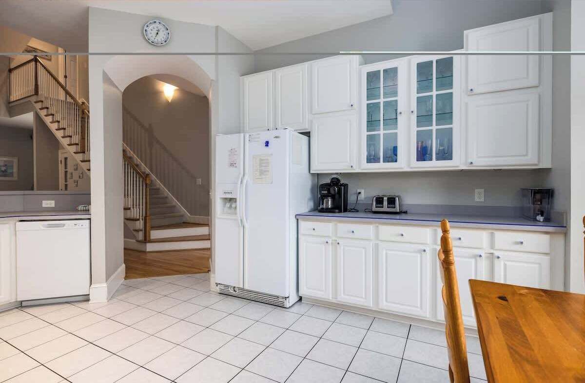 Una cocina con armarios blancos, un refrigerador, un microondas y una cafetera.