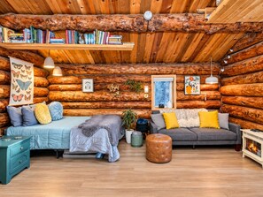 A log cabin interior with a bed, sofa, bookshelves, and a fireplace.