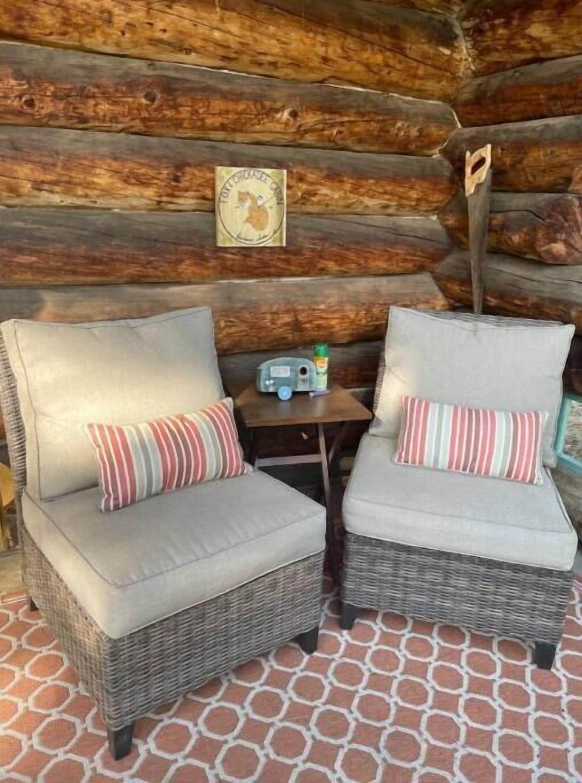 Deux fauteuils en osier avec des coussins et une petite table sur laquelle se trouvent une bouteille et une horloge.