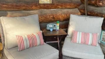 Deux fauteuils en osier avec des coussins et une petite table sur laquelle se trouvent une bouteille et une horloge.