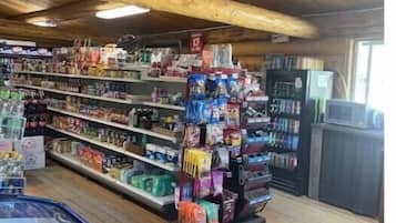 Una tienda con vigas de madera en el techo, estantes llenos de diversos productos y un mostrador refrigerado.