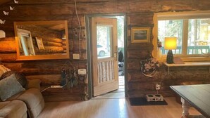 Interior acogedor de una cabaña de madera con piso de madera, un sofá, una mesa de comedor y un ventanal con vistas al exterior.