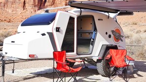 Un camping-car blanc avec un toit bleu, un logo rouge et deux chaises pliantes rouges.